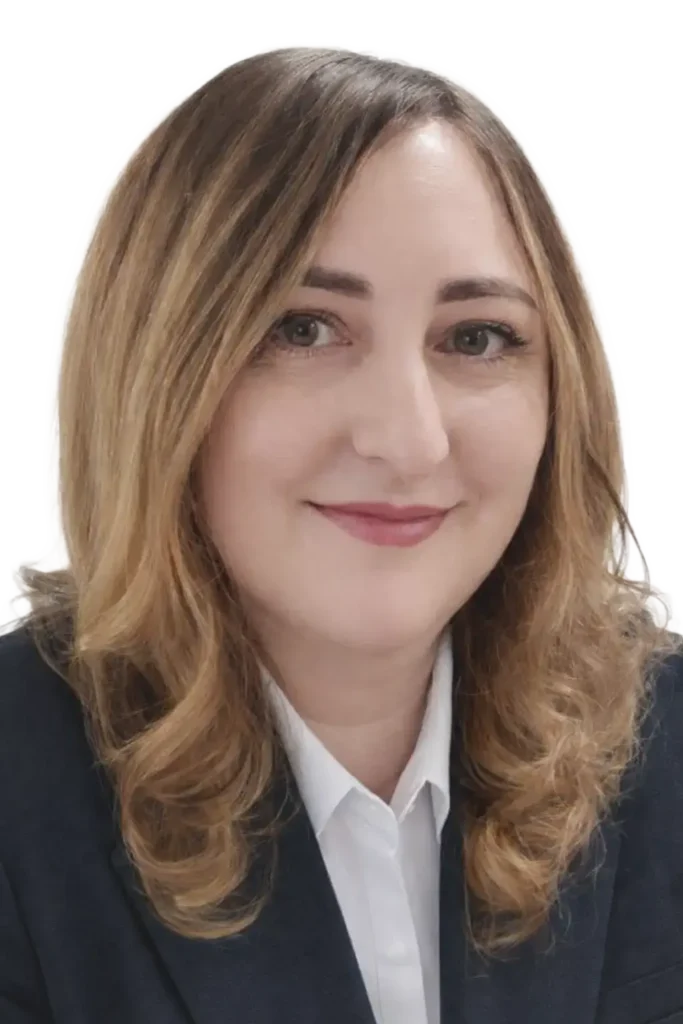 Portret uśmiechniętej kobiety w ciemnej marynarce i białej koszuli, z długimi jasnobrązowymi włosami